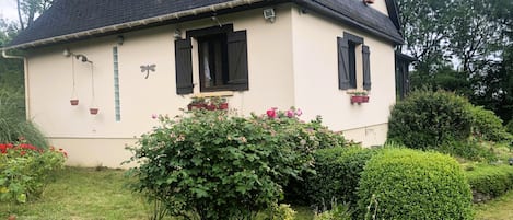 A house with a sloped roof, multiple windows with shutters, and a garden with various plants and flowers.
