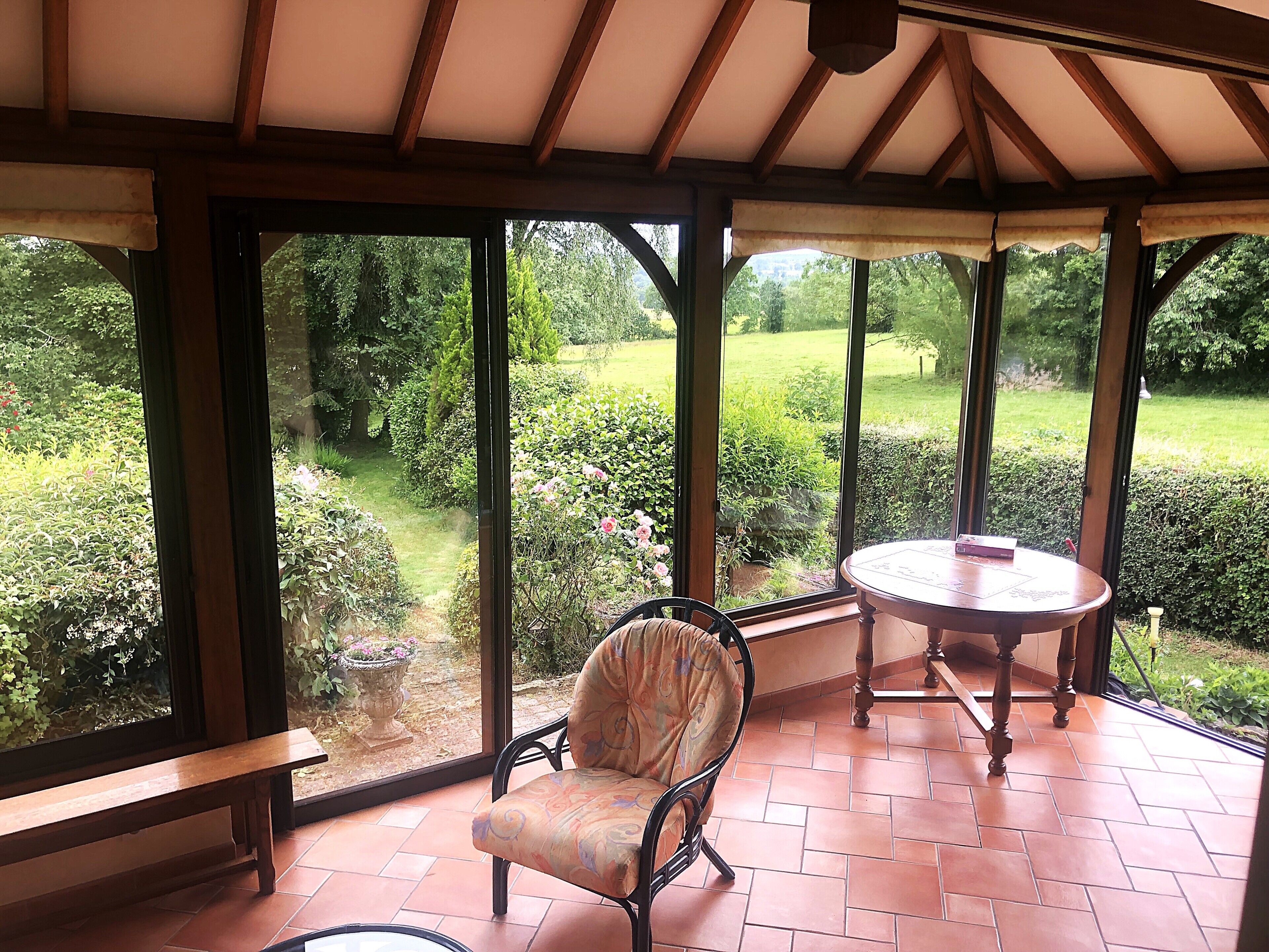A conservatory with a bench and a table, large windows offering a view of a garden.