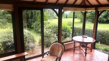 A conservatory with a bench and a table, large windows offering a view of a garden.