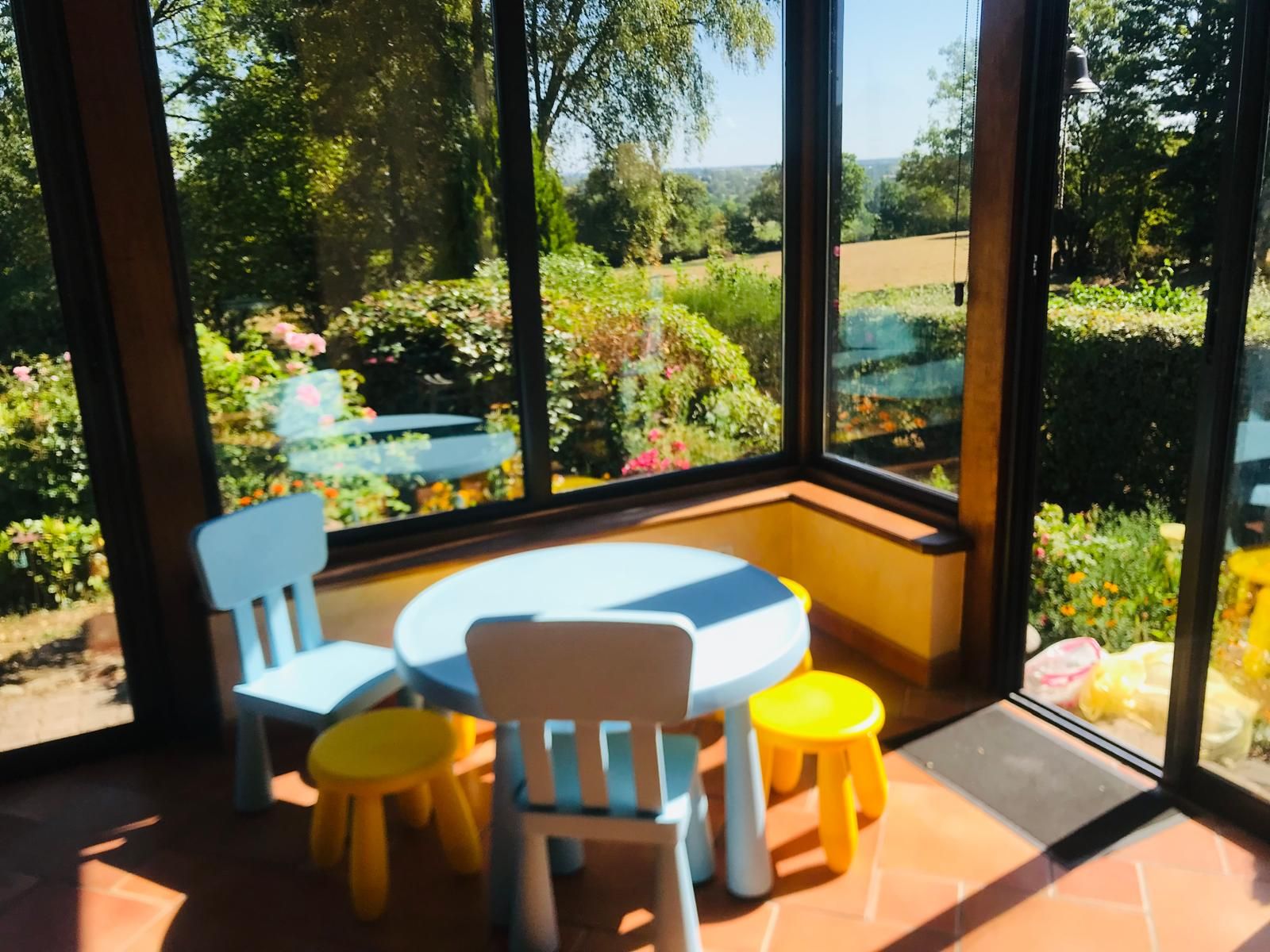 A room with a large window, a round table, two chairs, and two stools.