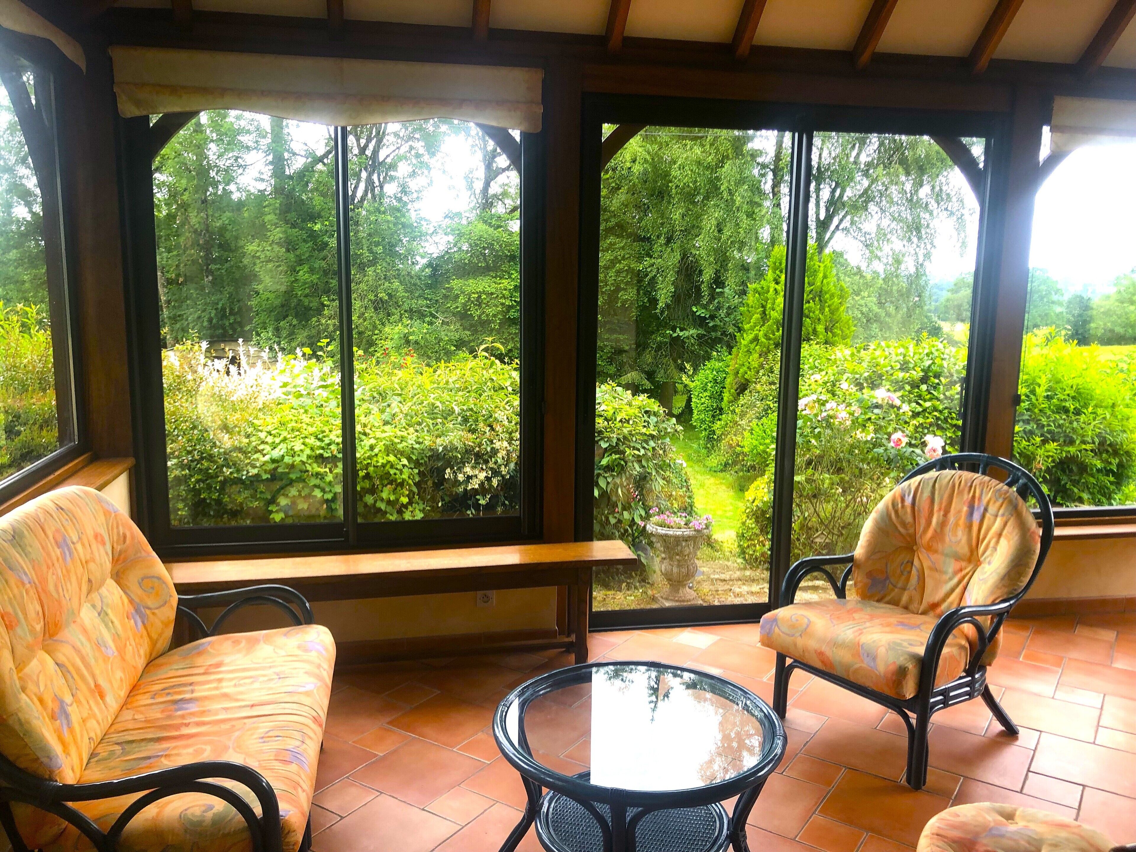 A conservatory with a bench, two chairs, and a glass table.