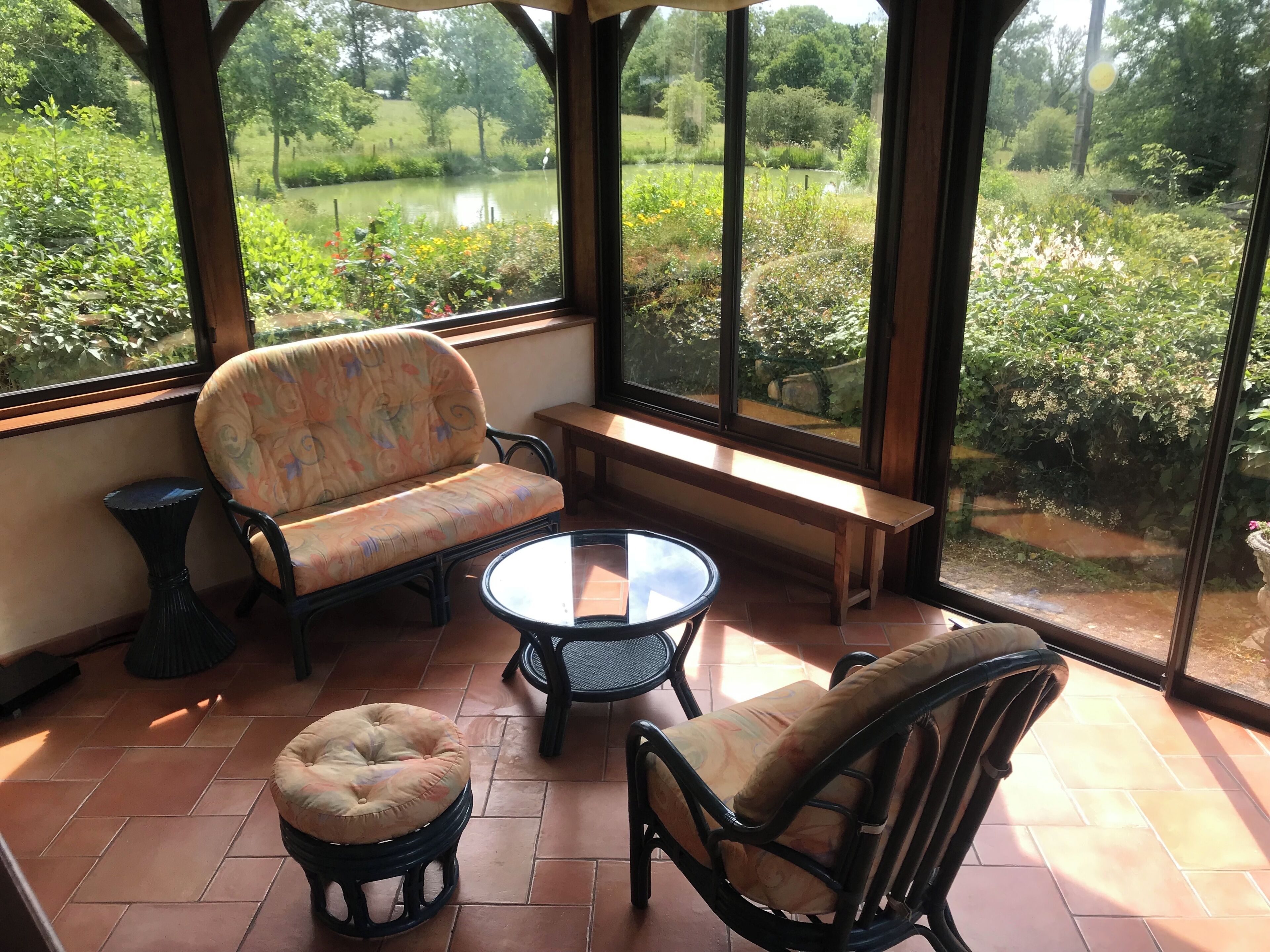 Een glazen ruimte met een bank, twee stoelen, een kleine tafel en een ronde poef.