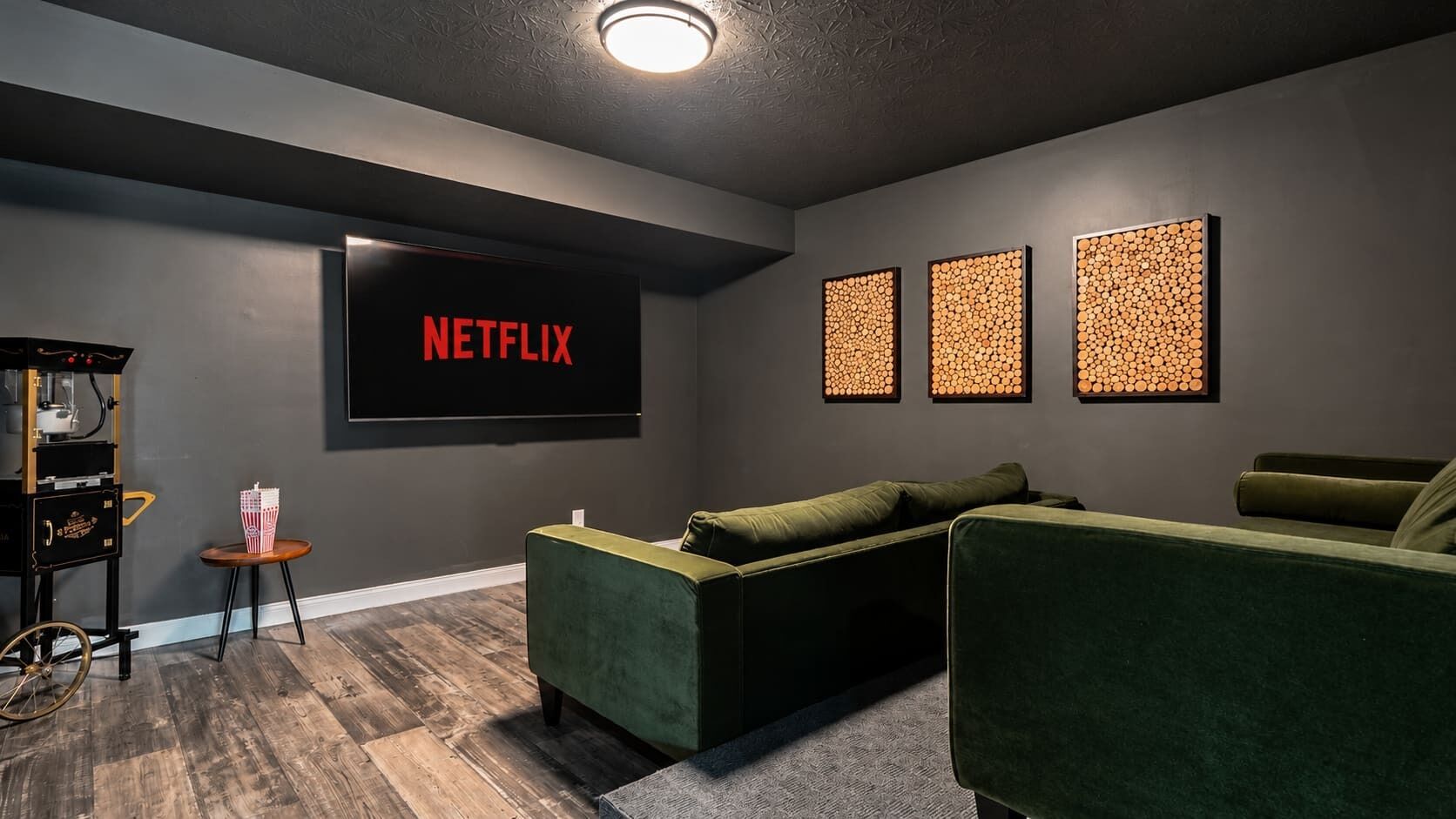 Un salon moderne doté d’un grand téléviseur à écran plat affichant le logo de Netflix, d’un appareil à pop-corn vintage et de trois œuvres d’art accrochées au mur.