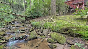 A forest stream with rocks and moss, a wooden deck, and a building with a staircase. - Little Creek Cabin — Sky Valley (Dillard)