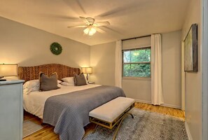 A bedroom with a bed, bedside lamps, a ceiling fan, a window with curtains, and a small rug. - Little Creek Cabin- Sky Valley (Dillard)