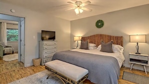 A bedroom with a bed, bedside lamps, a television, a ceiling fan, and a door leading to another room. - Little Creek Cabin — Sky Valley (Dillard)
