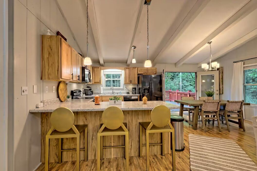 Une cuisine moderne avec des meubles en bois, un îlot central doté de tabourets, et un coin repas avec une table et des chaises.