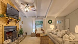 A cozy living room with a fireplace, a ceiling fan, a television, and a comfortable sofa. - Little Creek Cabin — Sky Valley (Dillard)