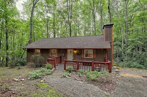 A cabin with a wooden exterior, a porch, and a chimney.