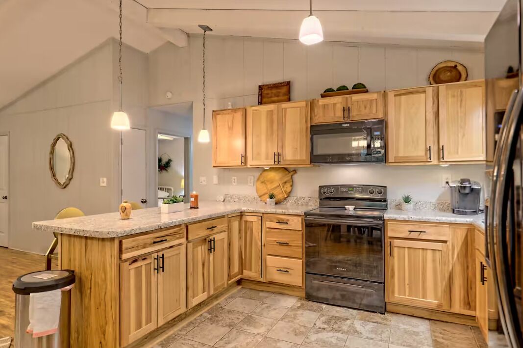 Une cuisine avec des meubles en bois, une cuisinière en acier inoxydable et des luminaires suspendus.