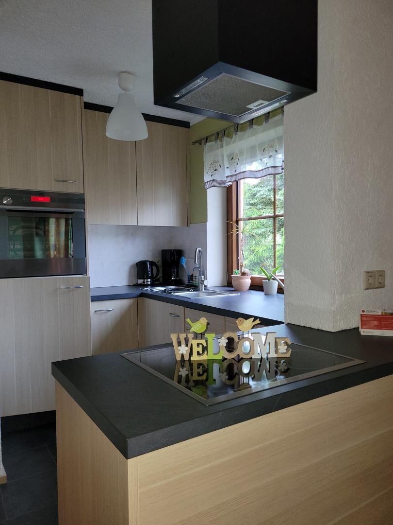 Eine moderne Küche mit Holzschränken, einem Einbauofen, einer Kaffeemaschine und einem Fenster mit Vorhängen.