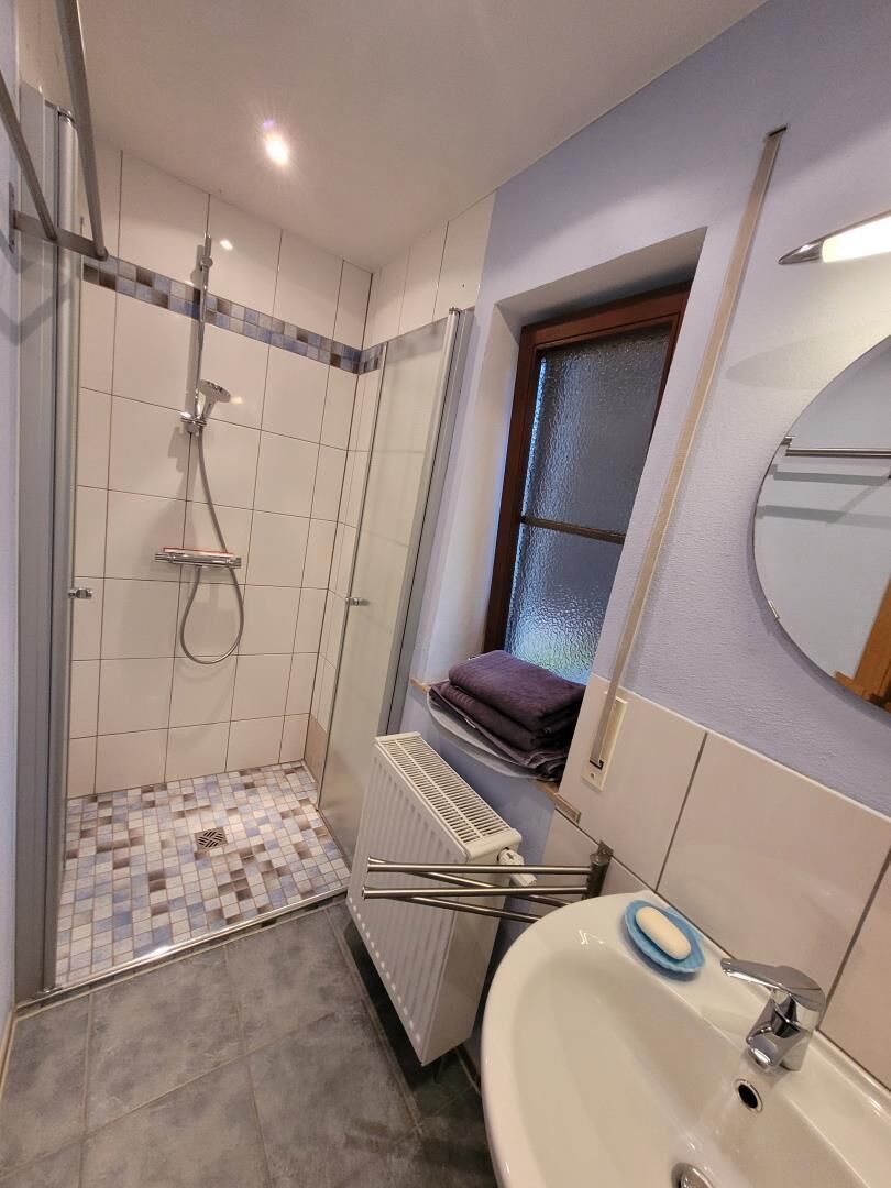 A bathroom with a shower, a sink, and a window.