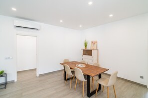 Un comedor moderno con una mesa de madera y seis sillas, una planta pequeña y un cuadro en un estante.