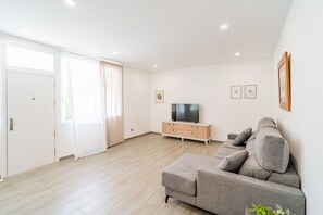 Ein modernes Wohnzimmer mit einem grauen Sofa, einem Fernseher auf einer Holzkassette und einer Schiebetür aus Glas.