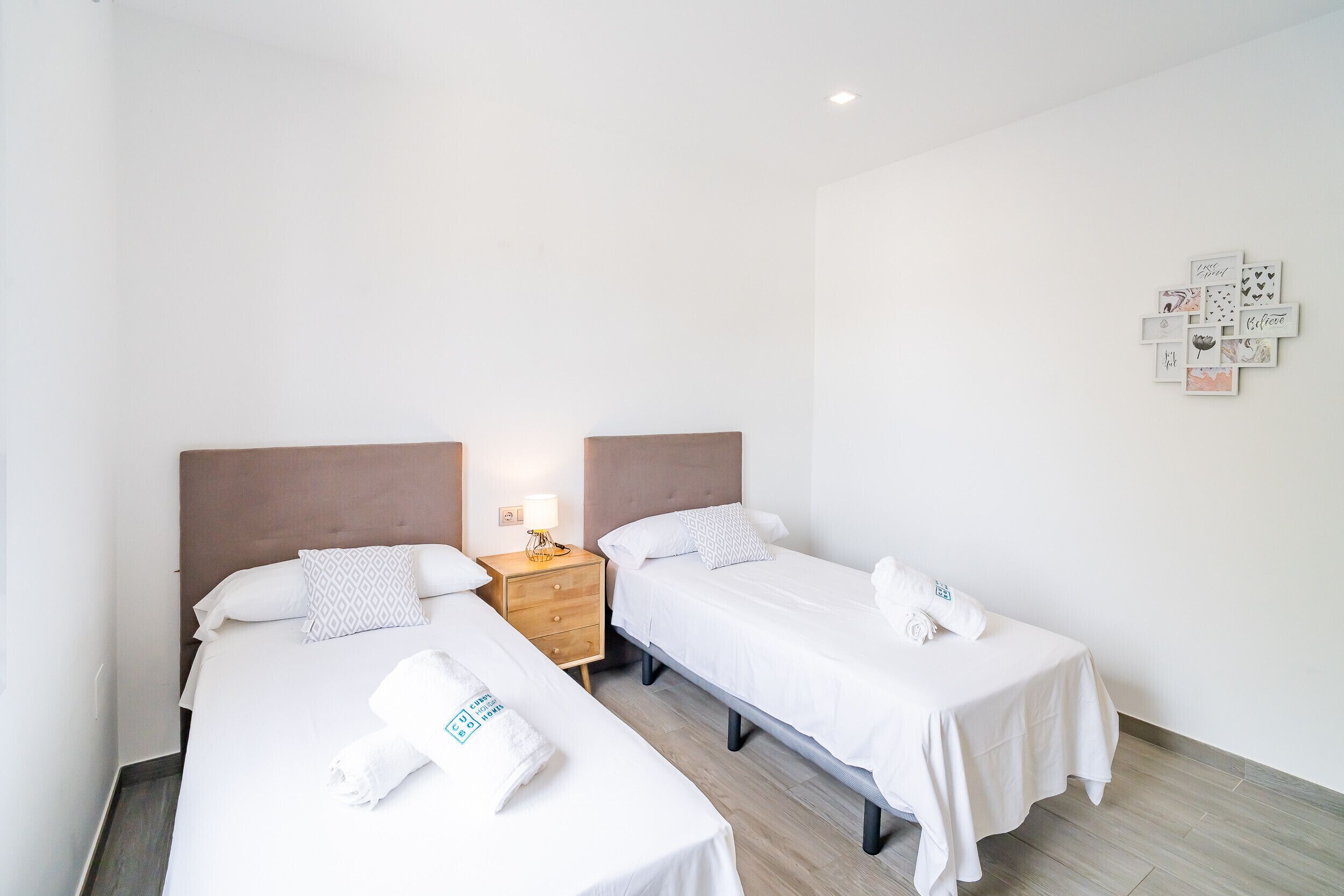 Habitación de hotel con dos camas individuales, una mesita de noche con lámpara y una pared con citas motivacionales.