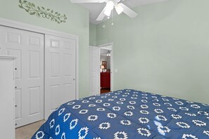 A bedroom with a bed, a white door, a ceiling fan, and a hallway leading to another room. - Private Courtyard Villa with All-Weather Lanai Near Brownwood (The Villages)