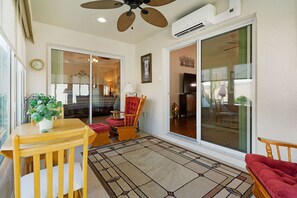 A sunlit room with a ceiling fan, a table with a plant, a red chair, and a large sliding glass door leading to another room. - Private Courtyard Villa with All-Weather Lanai Near Brownwood (The Villages)