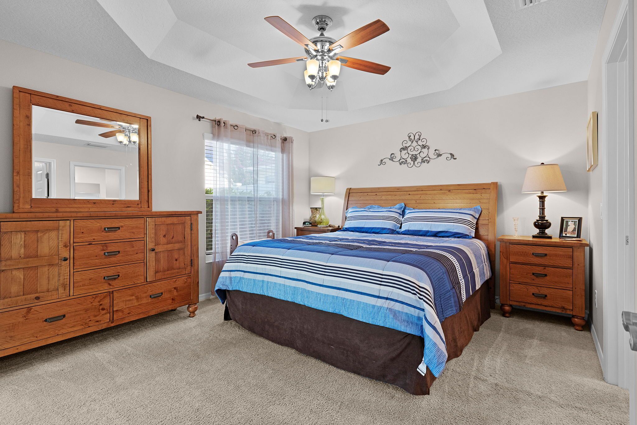A bedroom with a bed, a dresser, a nightstand, a ceiling fan, and a window with curtains.