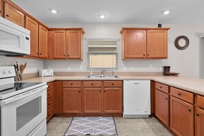 A kitchen with wooden cabinets, a built-in microwave, a toaster, a sink, and a dishwasher. - Private Courtyard Villa with All-Weather Lanai Near Brownwood (The Villages)
