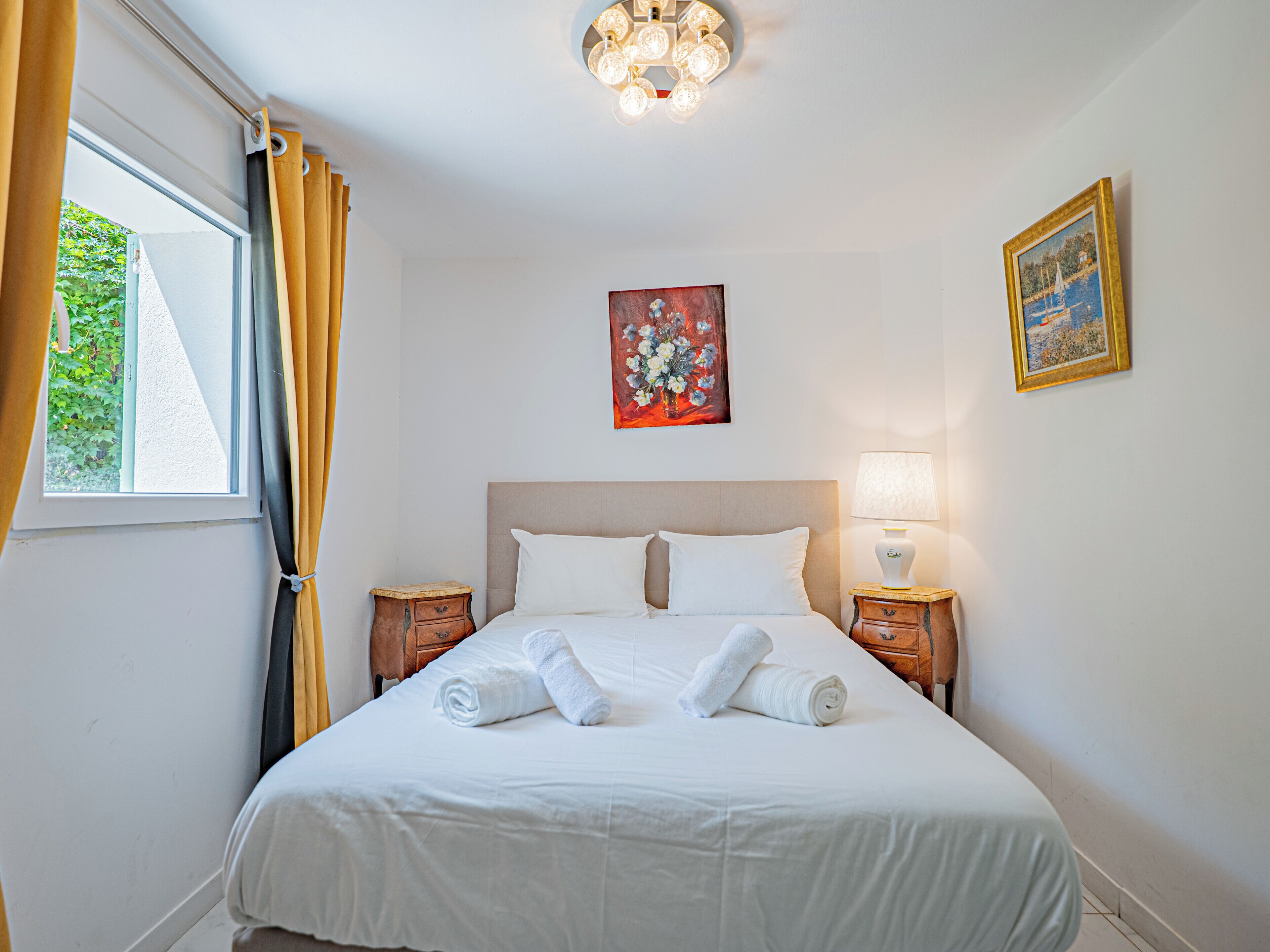 Une chambre d’hôtel avec un lit, deux tables de chevet, une fenêtre avec des rideaux et un tableau au mur.