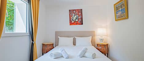 A hotel room with a bed, two nightstands, a window with curtains, and a painting on the wall.