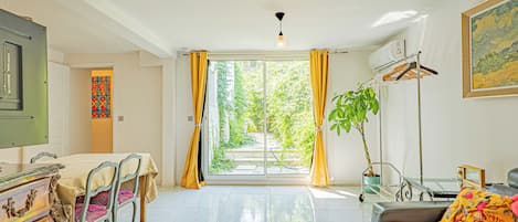 A room with a dining table, chairs, a sofa, a plant, and a painting on the wall.