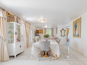 A dining area with a white table set for four, a cabinet with glass doors, and a painting on the wall. - La Maison Fleurs - Villa et jardin près de Cannes (Le Cannet)