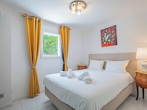 A hotel room with a bed, a nightstand, a lamp, a painting, and curtains. - La Maison Fleurs - Villa et jardin près de Cannes (Le Cannet)