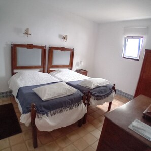 Uma cama de casal com cabeceiras de madeira, uma mesa de cabeceira com abajur e uma pequena janela.