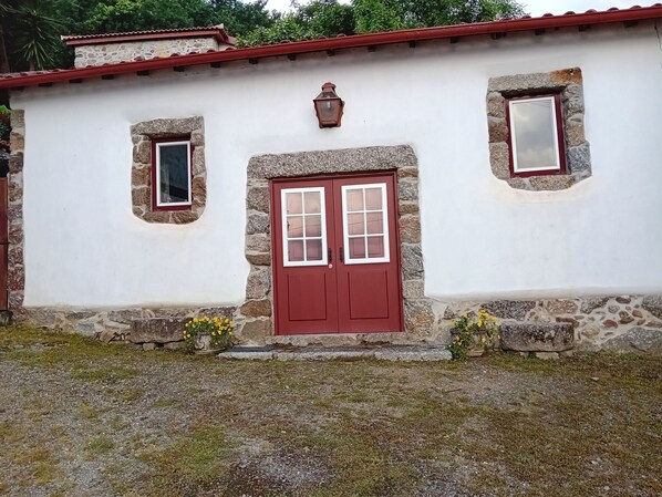 Um edifício rústico com porta vermelha, paredes de pedra e janelas pequenas.
