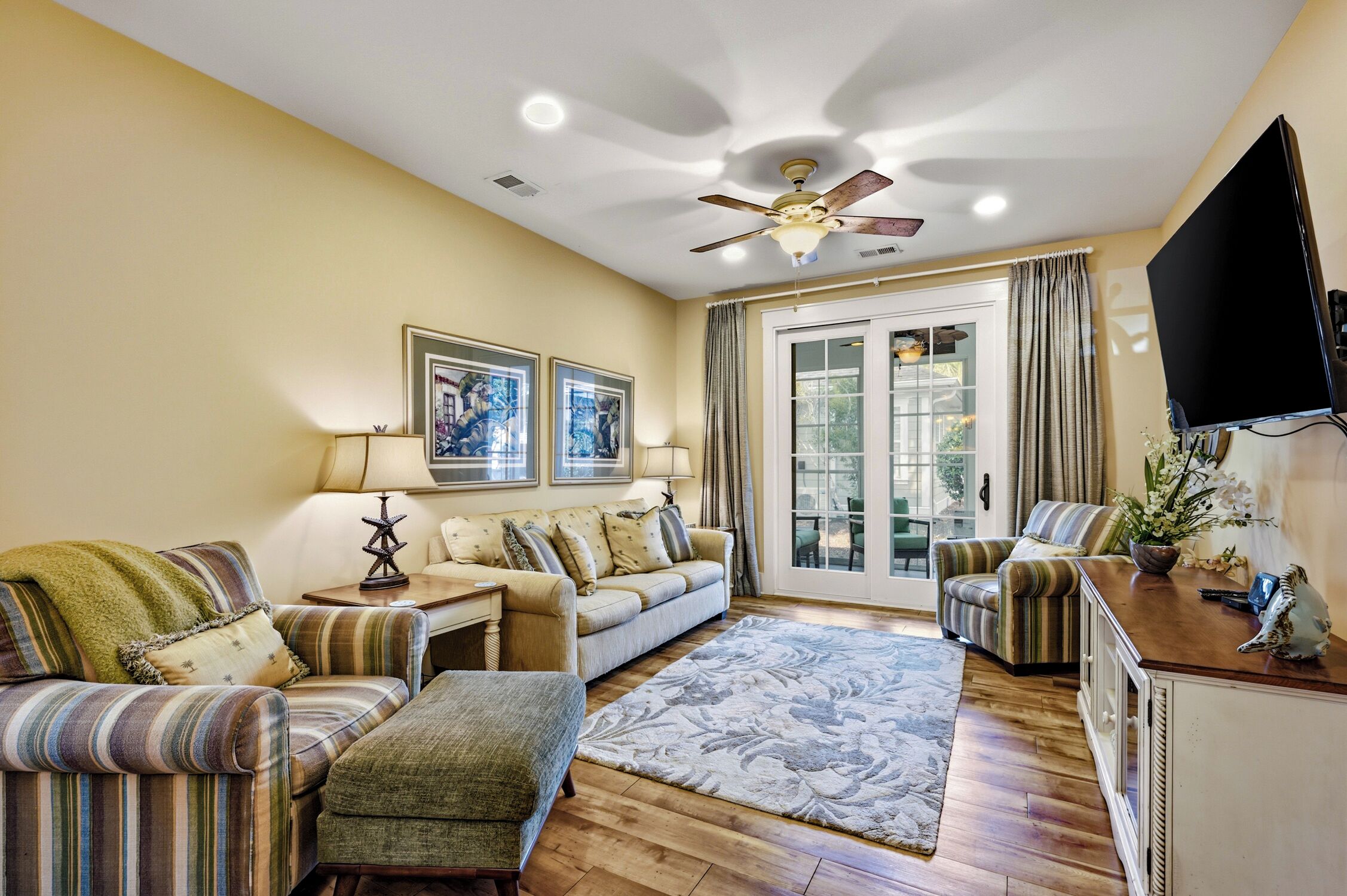 A living room with a sofa set, a coffee table, a rug, a ceiling fan, and a television.