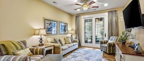 A living room with a sofa set, a coffee table, a rug, a ceiling fan, and a television.
