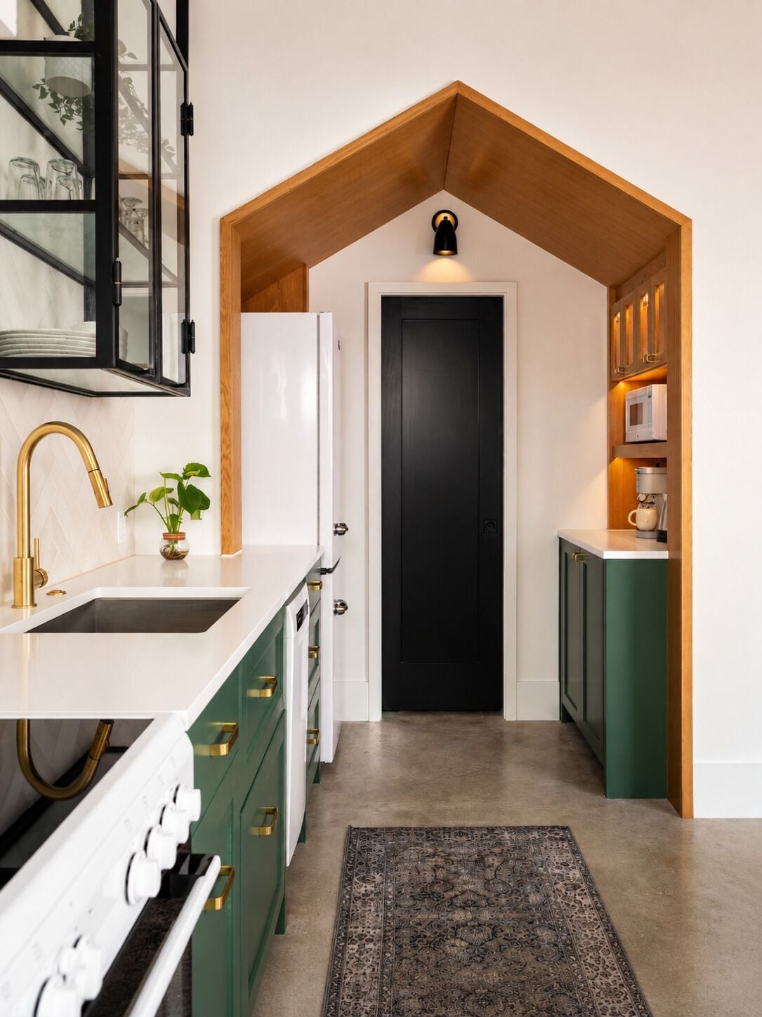 A kitchen with a white countertop, a gold faucet, a black door, and a green cabinet.