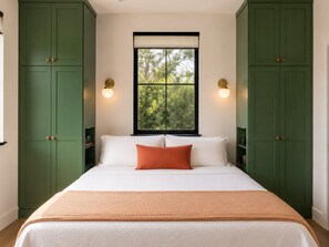 Ein Schlafzimmer mit einem Bett, grünen Schränken, einem Fenster und Wandleuchten.