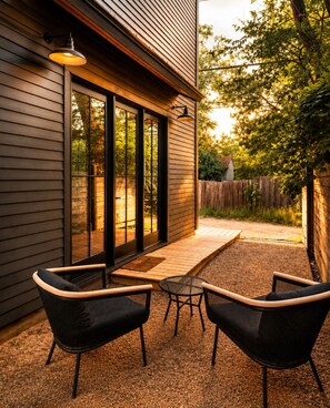 Une terrasse extérieure avec deux chaises et une table, une terrasse en bois et une maison dont le revêtement extérieur est de couleur sombre.