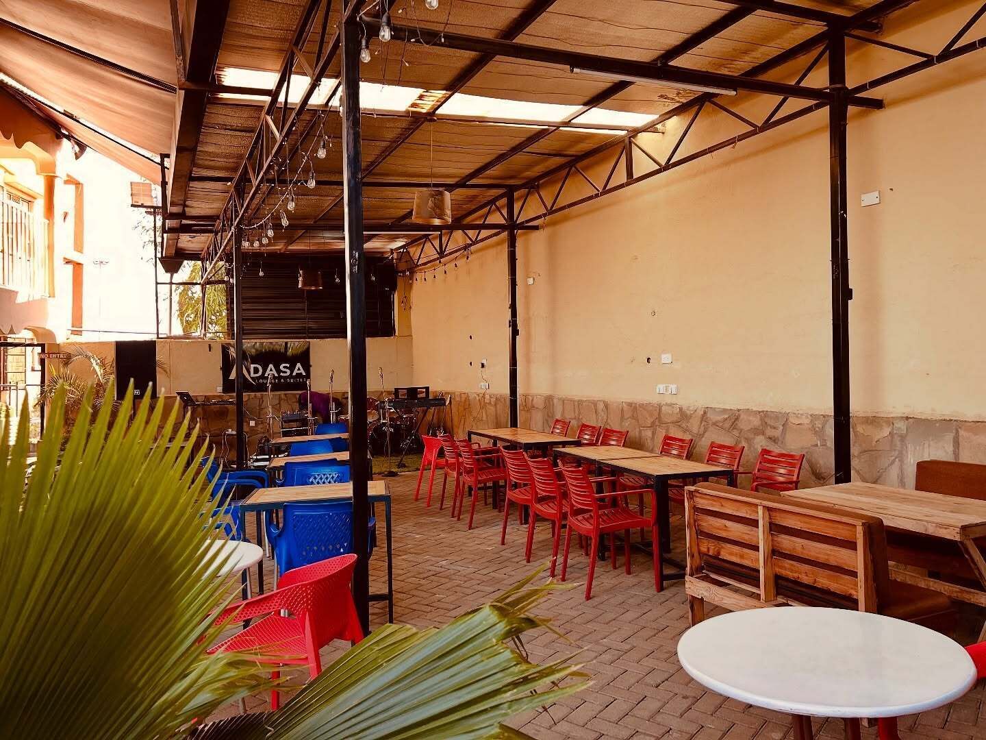 An outdoor seating area with tables and chairs, a stage with musical instruments, and a sign for 'DASA Lounge & Suites'.
