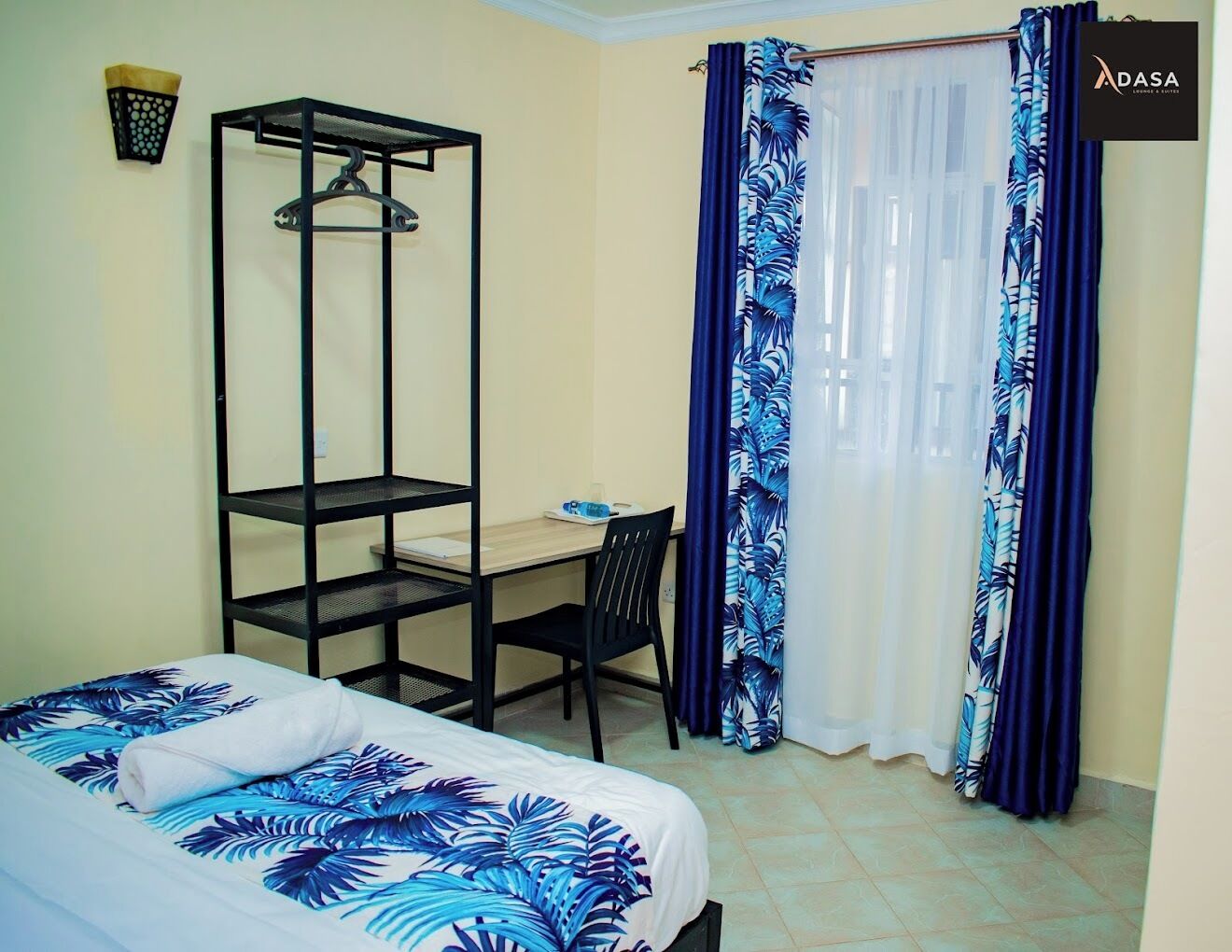 A bedroom with a bed, a desk, a chair, a wardrobe, and a window with curtains.
