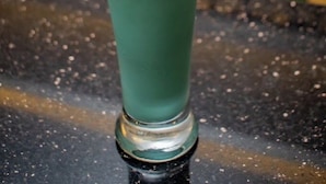 A tall glass with a green beverage, a straw, and an orange slice garnish on a bar counter. - Adasa Lounge and Suites (Kisumu)