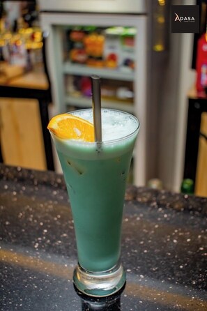 Un grand verre contenant une boisson verte, une paille et une tranche d’orange en guise de décoration, posé sur le comptoir d’un bar.