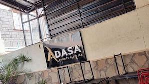 A building with a sign for 'ADASA Lounge & Suites' and outdoor seating with chairs and tables. - Adasa Lounge and Suites (Kisumu)