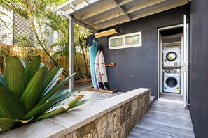 Un área de lavandería con lavadora y secadora, un banco de madera y un soporte para tablas de surf.