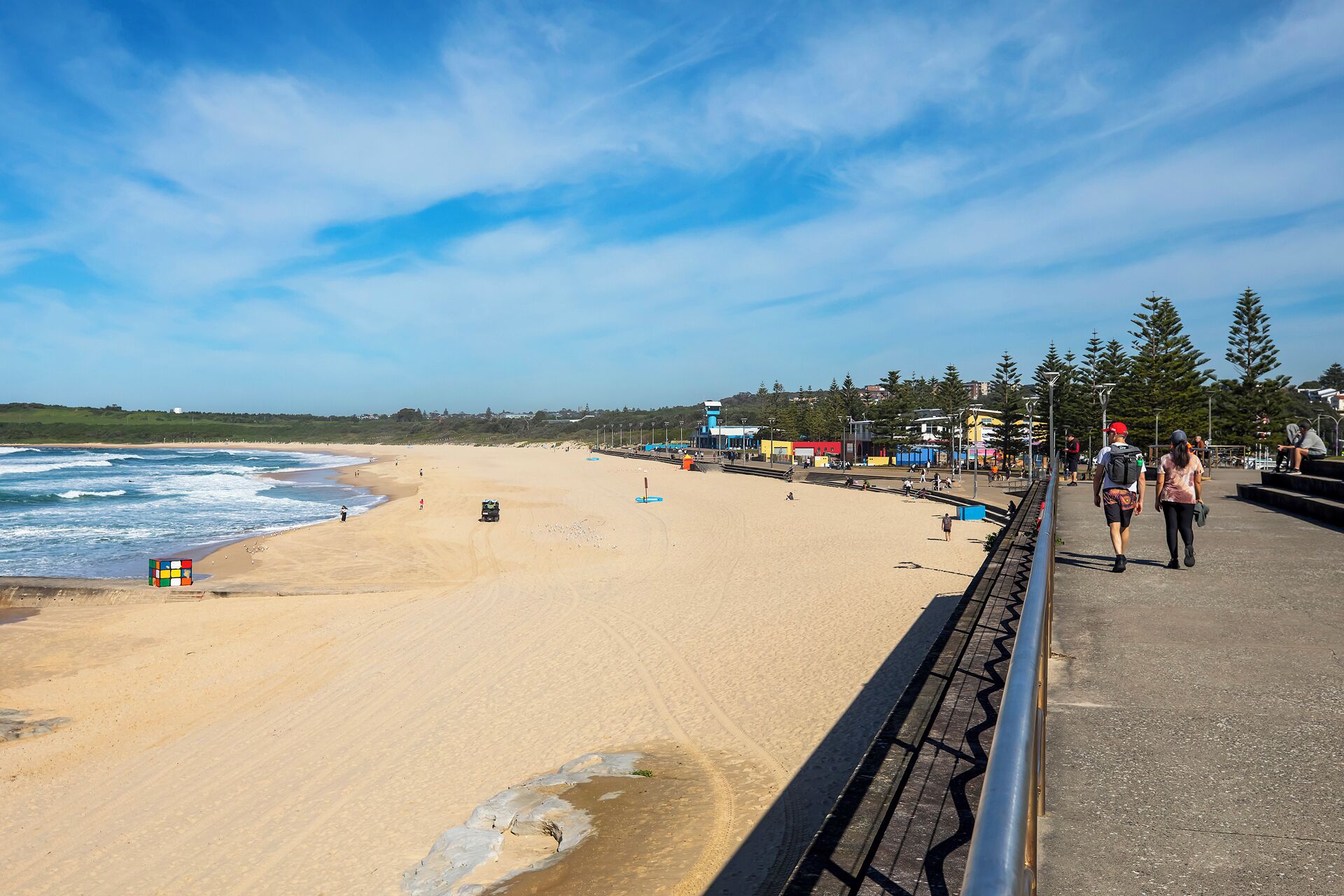 A beach with a clear sky, a sandy shore, and a pedestrian walkway.