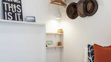 A bedroom with a bed, a wall-mounted hat rack, a shelf with hats, a framed sign, and a blanket.
