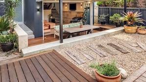 Uma casa moderna de dois andares com um alpendre coberto, área de estar externa e vasos de plantas.
