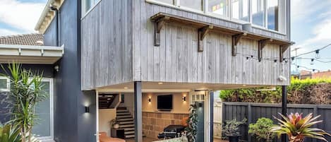A modern two-story house with a covered patio area, outdoor seating, and potted plants.