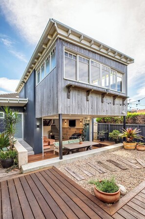 Ein modernes, zweistöckiges Haus mit überdachter Terrasse, Sitzgelegenheiten im Freien und Blumentöpfen.