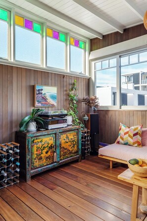 Ein Zimmer mit Holzboden, einem Holzschrank mit Dekoration, einer Couch mit gemusterten Kissen und einem großen Fenster mit Blick auf Gebäude.