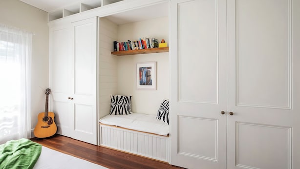Um quarto com cama, um violão, uma estante de livros e uma janela com cortinas.