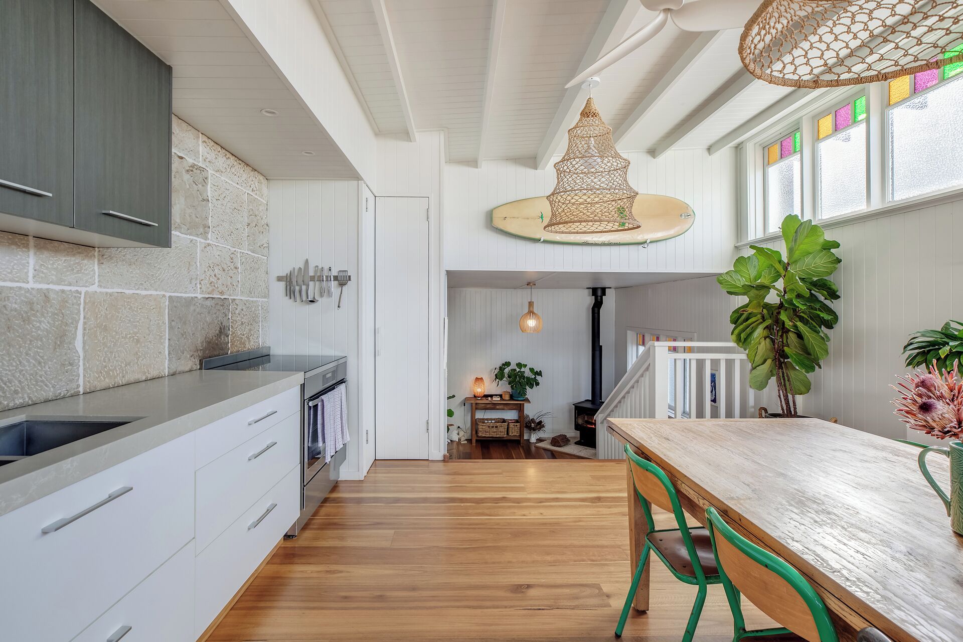 A modern kitchen with white cabinetry, a wooden dining table, and a hanging light fixture.