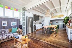 A modern kitchen with a large refrigerator, a dining area with a wooden table and chairs, and a sofa with cushions. - Maroubra Escape Beachside Charm and Ocean Glimpses (Maroubra)